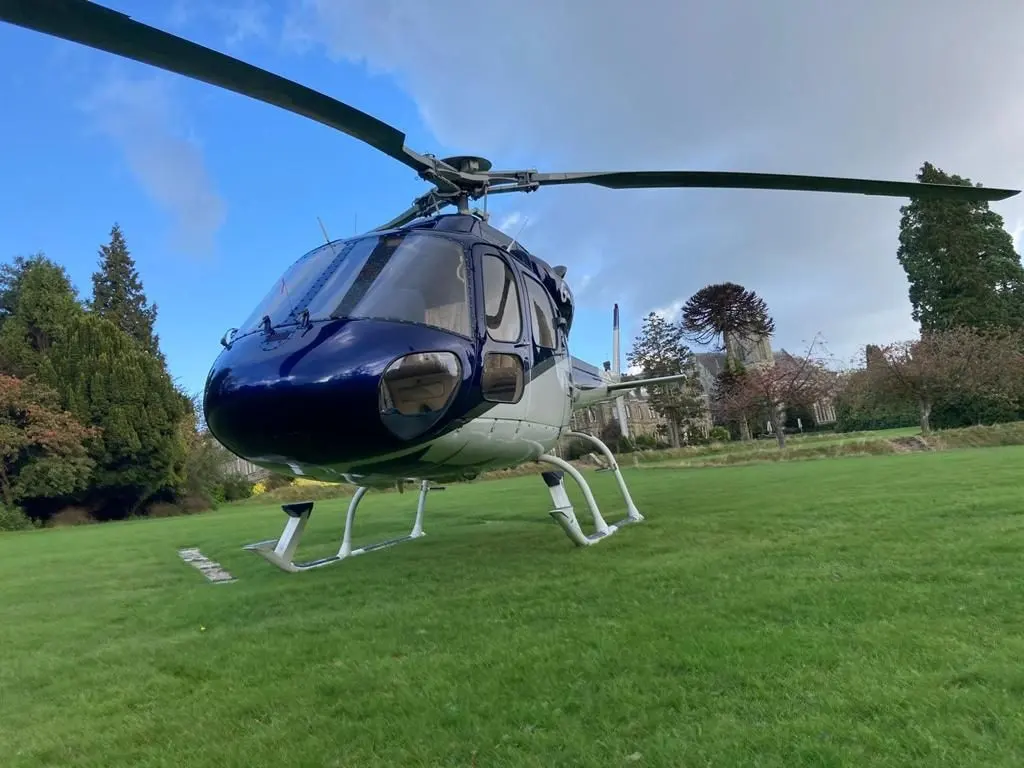 A blue and white light helicopter on a lawn with trees behind