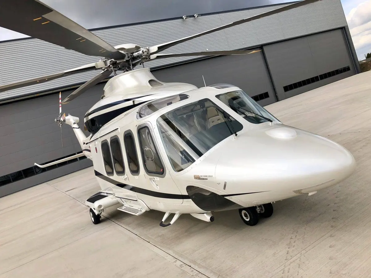 A white twin-engine helicopter parked on concrete in front of a hangar