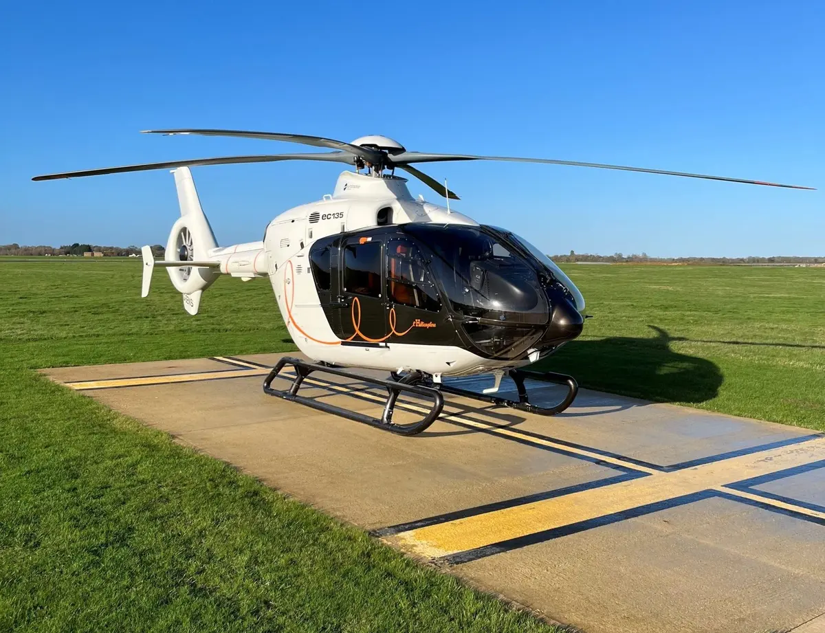 A white helicopter with a black cabin on a concrete pad with yellow markings
