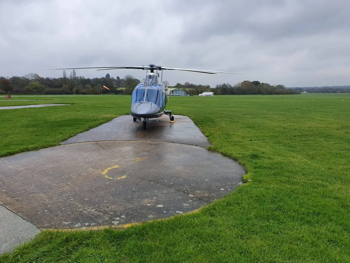 A helicopter on a small concrete pad surrounded by wet grass