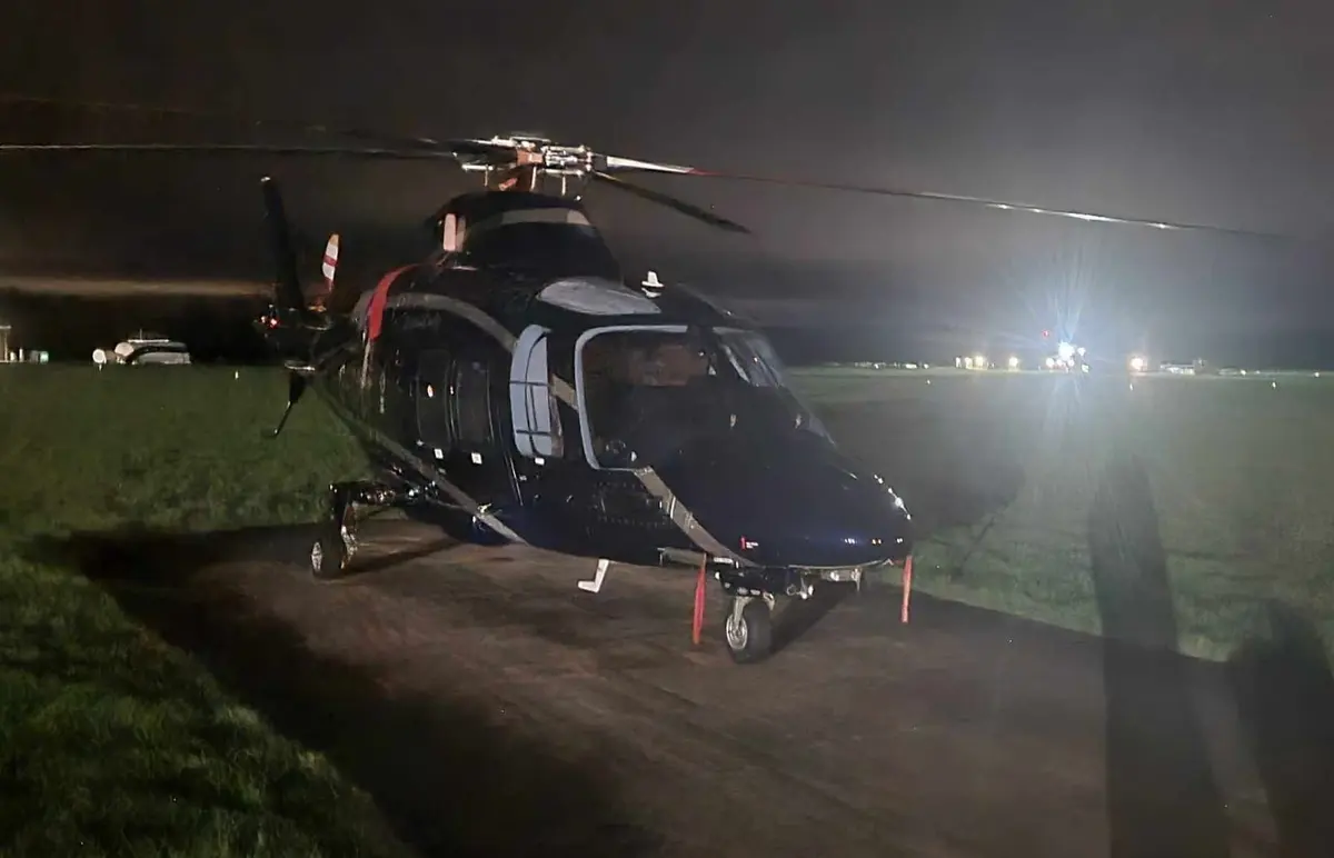 A helicopter on a grass airfield at night with a bright lamp and distant edge lights